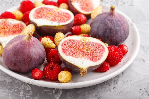 Fresh figs, strawberries and raspberries on white ceramic plate on gray concrete background. side