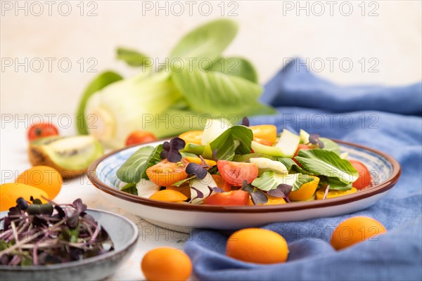 Vegetarian salad of pac choi cabbage, kiwi, tomatoes, kumquat, microgreen sprouts on a white