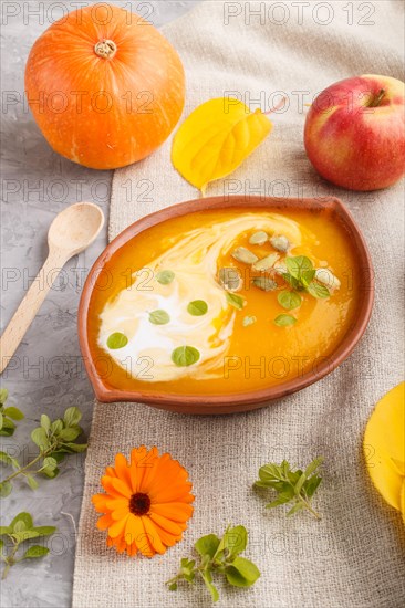 Traditional pumpkin cream soup with seeds in clay bowl on a gray concrete background with linen