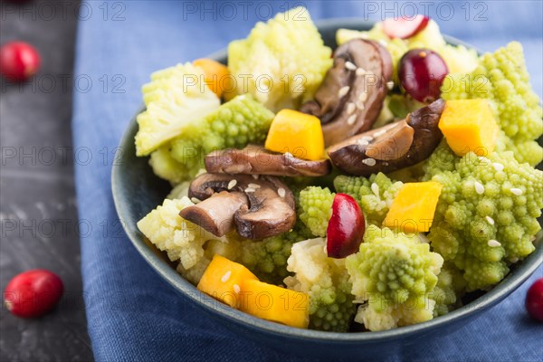 Vegetarian salad from romanesco cabbage, champignons, cranberry, avocado and pumpkin on a black