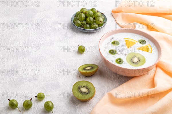 Yogurt with kiwi, gooseberry, chia in ceramic bowl on gray concrete background and orange linen