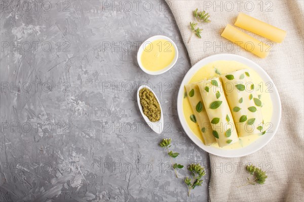 Cannelloni pasta with egg sauce, cream cheese and oregano leaves on a gray concrete background with