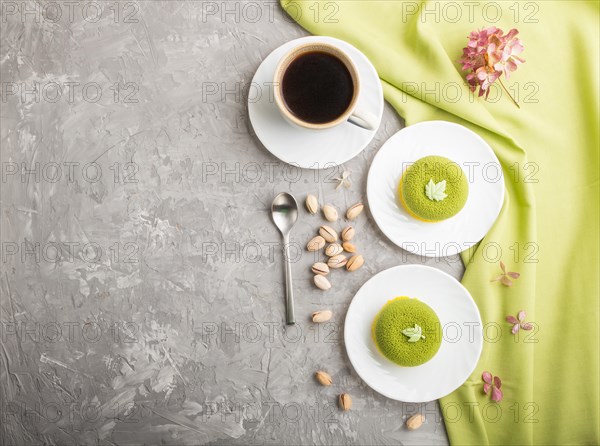 Green mousse cake with pistachio cream and a cup of coffee on a gray concrete background and green