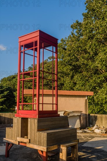 Red wooden telephone booth minus phone and without glass on roof of building on sunny day with blue