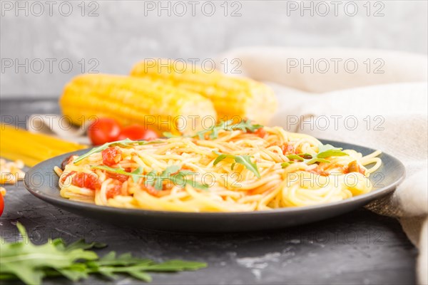 Corn noodles with tomato sauce and arugula on a black concrete background and linen textile. Side