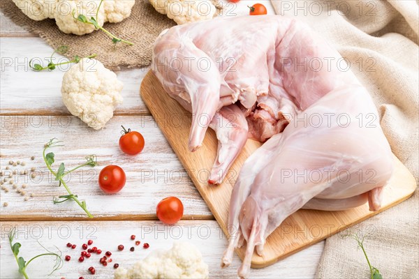 Whole raw rabbit with cauliflower, tomatoes and spices on a white wooden background and linen