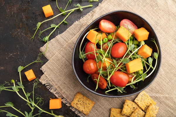 Vegetarian vegetable salad of tomatoes, pumpkin, microgreen pea sprouts on black concrete