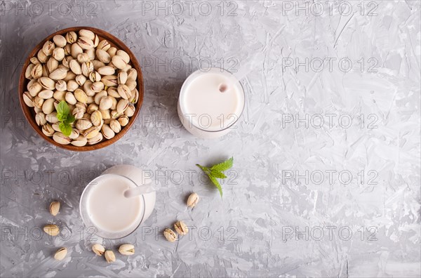 Organic non dairy pistachio milk in glass and wooden plate with pistachionuts on a gray concrete