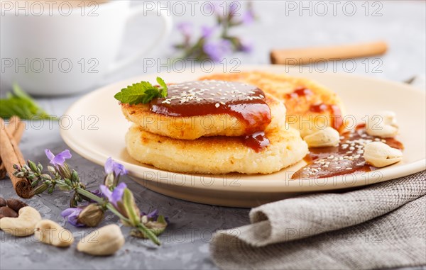 Cheese pancakes with caramel sauce on a beige ceramic plate and a cup of coffee on a gray concrete
