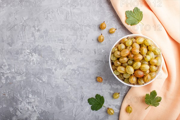 Fresh green gooseberry in white bowl with orange textile on gray concrete background. top view,
