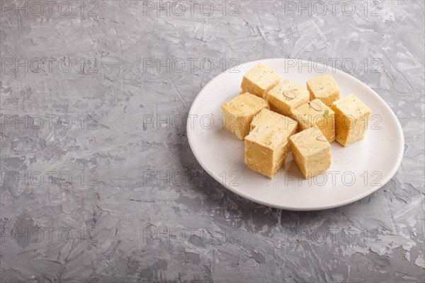 Traditional indian candy soan papdi in white plate with almond and pistache on a gray concrete
