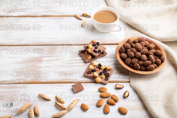 Almond in chocolate dragees in wooden plate and a cup of coffee on white wooden background and