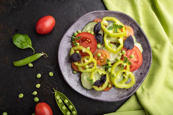 Vegetarian salad from green pea, tomatoes, pepper and basil on a black concrete background and