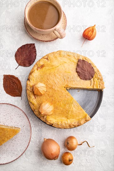 Autumn onion pie decorated with leaves and cup of coffee on gray concrete background. Top view,