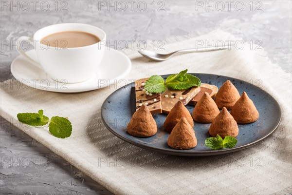 Chocolate truffle on blue ceramic plate and a cup of coffee on gray concrete background. close up,