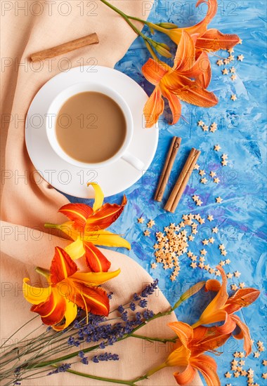 Orange day-lily and lavender flowers and a cup of coffee on a blue concrete background, with orange
