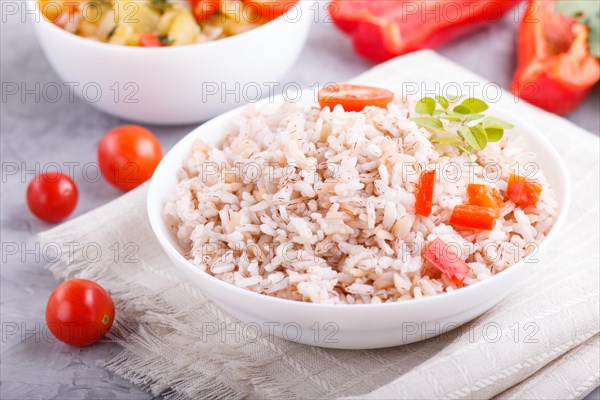 Unpolished rice porridge with stewed vegetables and oregano in white bowl on a gray concrete
