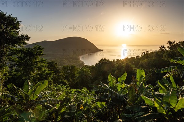 View from a mountain to a secluded bay with a sandy beach and mangrove forest. The sun rises over