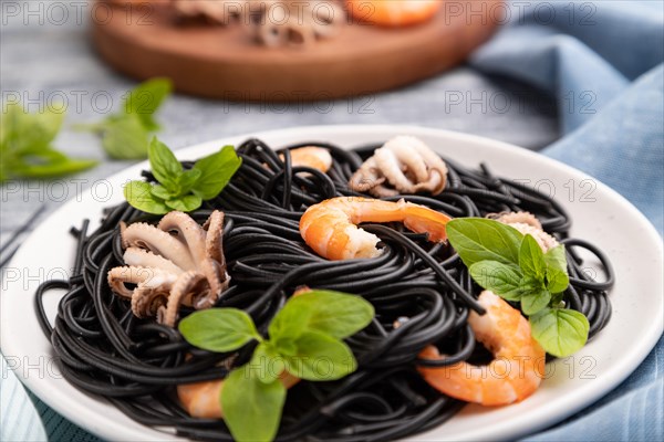 Black cuttlefish ink pasta with shrimps or prawns and small octopuses on gray wooden background and
