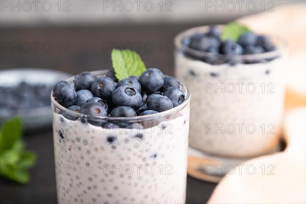 Yogurt with blueberry and chia in glass on black concrete background and orange linen textile. Side