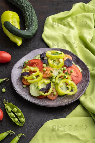 Vegetarian salad from green pea, tomatoes, pepper and basil on a black concrete background and