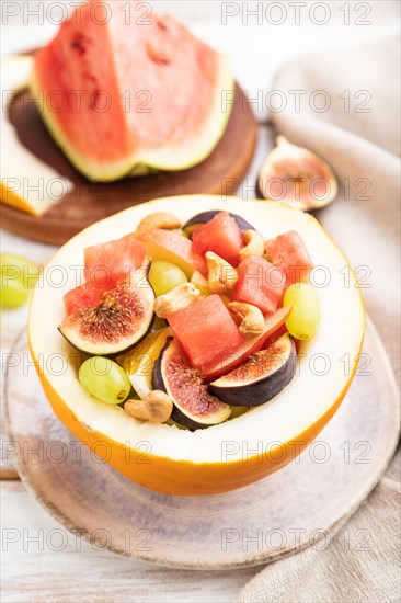Vegetarian fruit salad of watermelon, grapes, figs, pear, orange, cashew on white wooden background