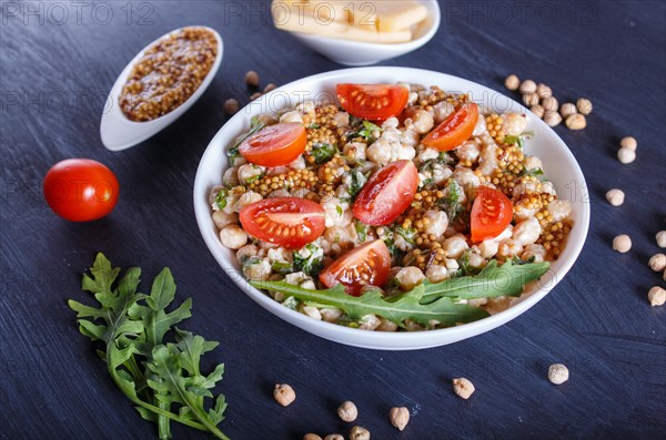 Vegetarian salad of boiled chickpeas, cheese, arugula, mustard and cherry tomatoes on black wooden