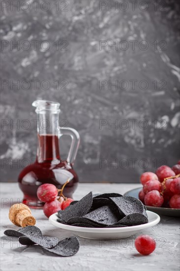Black potato chips with charcoal, balsamic vinegar in glass, red grapes on a blue ceramic plate on