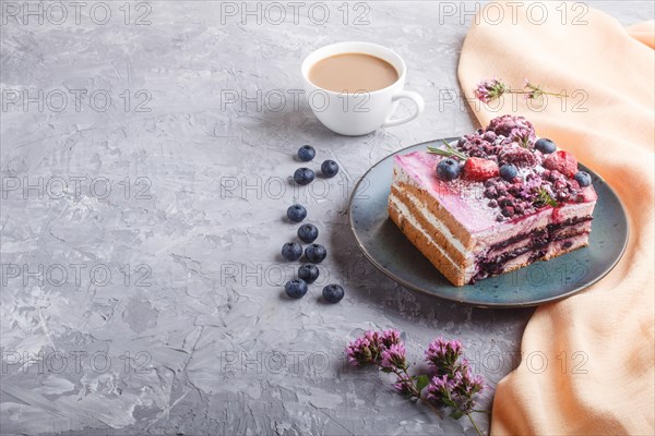 Berry cake with milk cream and blueberry jam on blue ceramic plate with cup of coffee and fresh