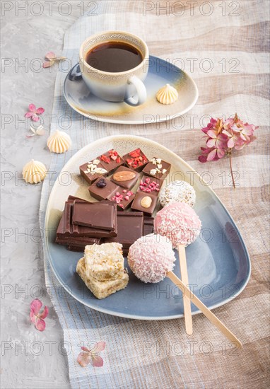 A pieces of homemade chocolate with coconut candies and a cup of coffee on a gray concrete