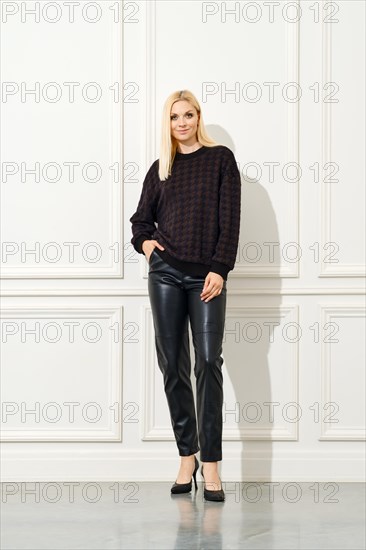A stylish woman standing against a white, panelled wall. She is dressed in a dark, patterned