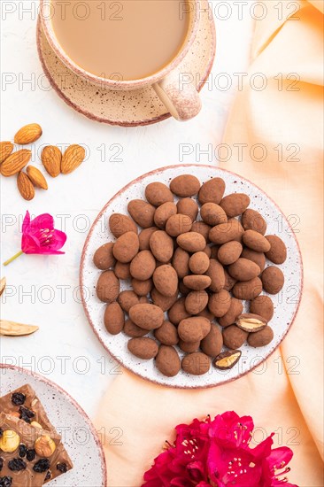 Almond in chocolate dragees on ceramic plate and a cup of coffee on white concrete background and