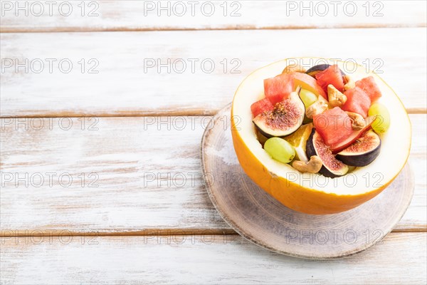 Vegetarian fruit salad of watermelon, grapes, figs, pear, orange, cashew on white wooden background