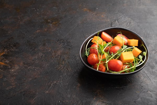 Vegetarian vegetable salad of tomatoes, pumpkin, microgreen pea sprouts on black concrete