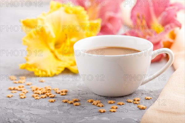 Yellow anf purple day-lilies cup of coffee on a gray concrete background, with orange textile.