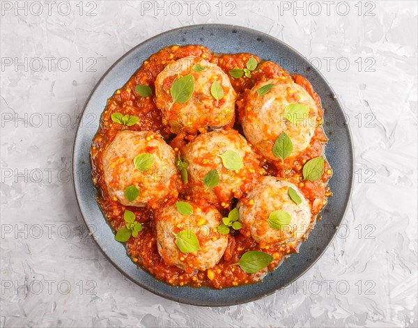 Pork meatballs with tomato sauce, oregano leaves, spices and herbs on blue ceramic plate on a gray