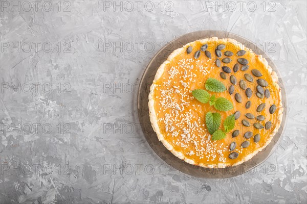 Traditional american sweet pumpkin pie decorated with mint, sesame and pumpkin seeds on a gray