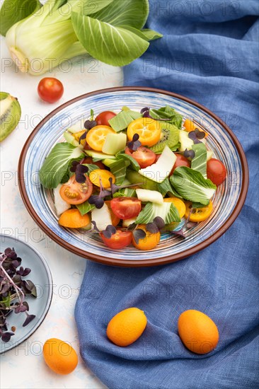 Vegetarian salad of pac choi cabbage, kiwi, tomatoes, kumquat, microgreen sprouts on a white
