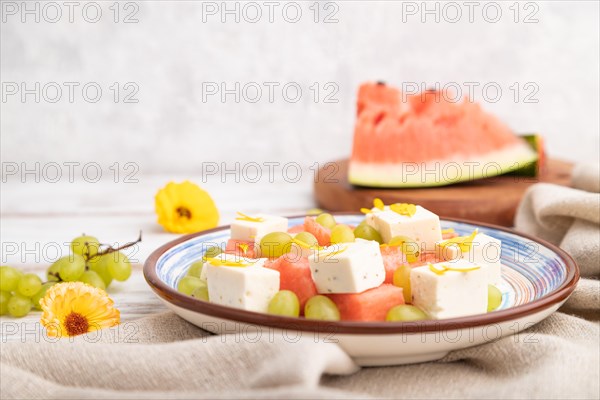 Vegetarian salad with watermelon, feta cheese, and grapes on blue ceramic plate on white wooden