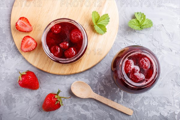 Strawberry jam in a glass jar with berries and leaves on gray concrete background. Homemade, top