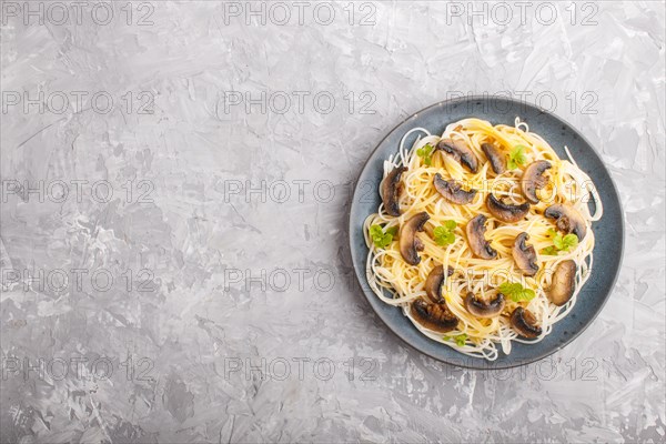 Rice noodles with champignons mushrooms, egg sauce and oregano on blue ceramic plate on a gray