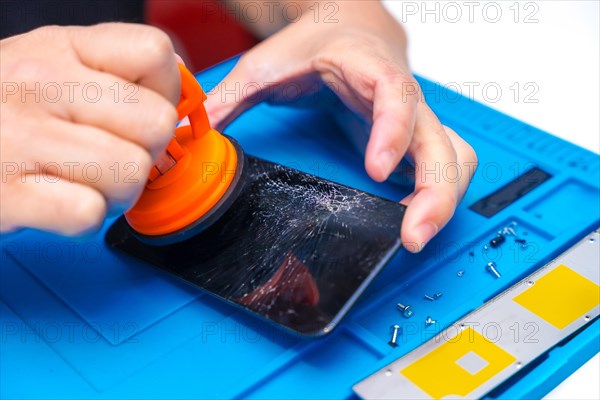 Close-up of the hands of a repairman using a suction cup to lift a broken screen of a mobile phone