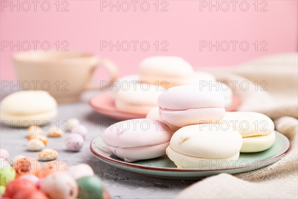 Colored zephyr or marshmallow with cup of coffee and dragees on a gray and pink background and