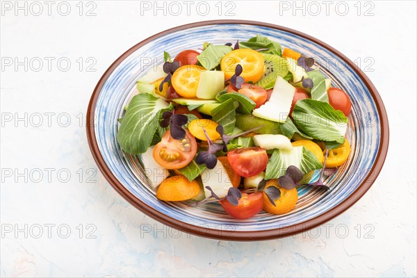 Vegetarian salad of pac choi cabbage, kiwi, tomatoes, kumquat, microgreen sprouts on a white