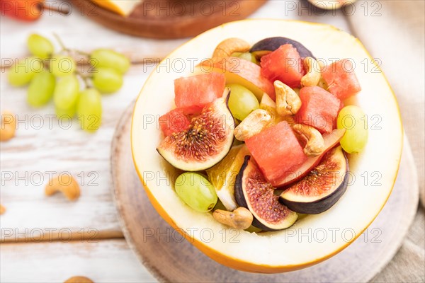 Vegetarian fruit salad of watermelon, grapes, figs, pear, orange, cashew on white wooden background