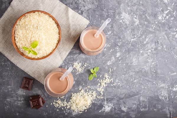 Organic non dairy rice chocolate milk in glass and wooden plate with rice seeds on a black concrete