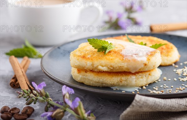 Cheese pancakes on a blue ceramic plate and a cup of coffee on a gray concrete background. side