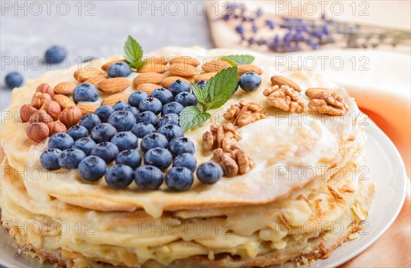 Homemade layered Napoleon cake with milk cream. Decorated with blueberry, almonds, walnuts,