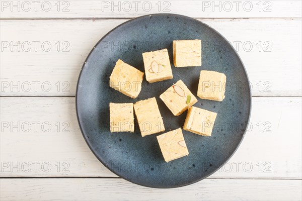 Traditional indian candy soan papdi in a blue ceramic plate with almond and pistache on a white
