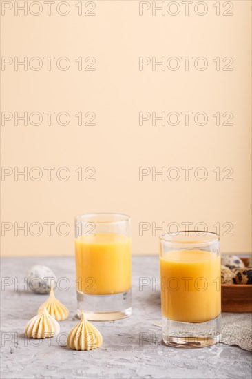 Sweet egg liqueur in glass with quail eggs and meringues on a gray and orange background. Side